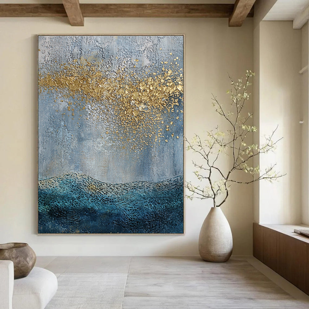 Large abstract painting with a textured sky-blue gray background and golden highlights featuring a textured sea with gentle waves in the foreground.STSC835