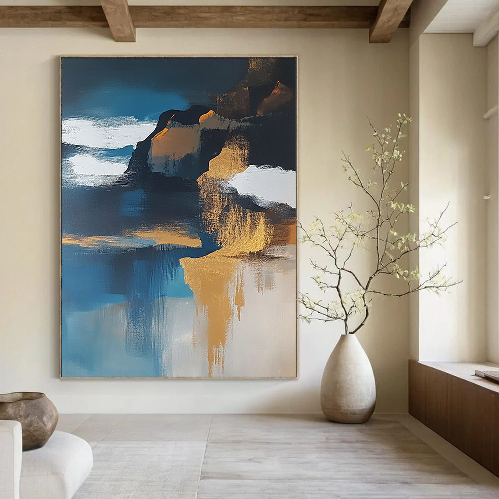 Large abstract painting of an island featuring navy blue water white clouds brown sand and gold leafing exuding a sense of calmness.STSC651