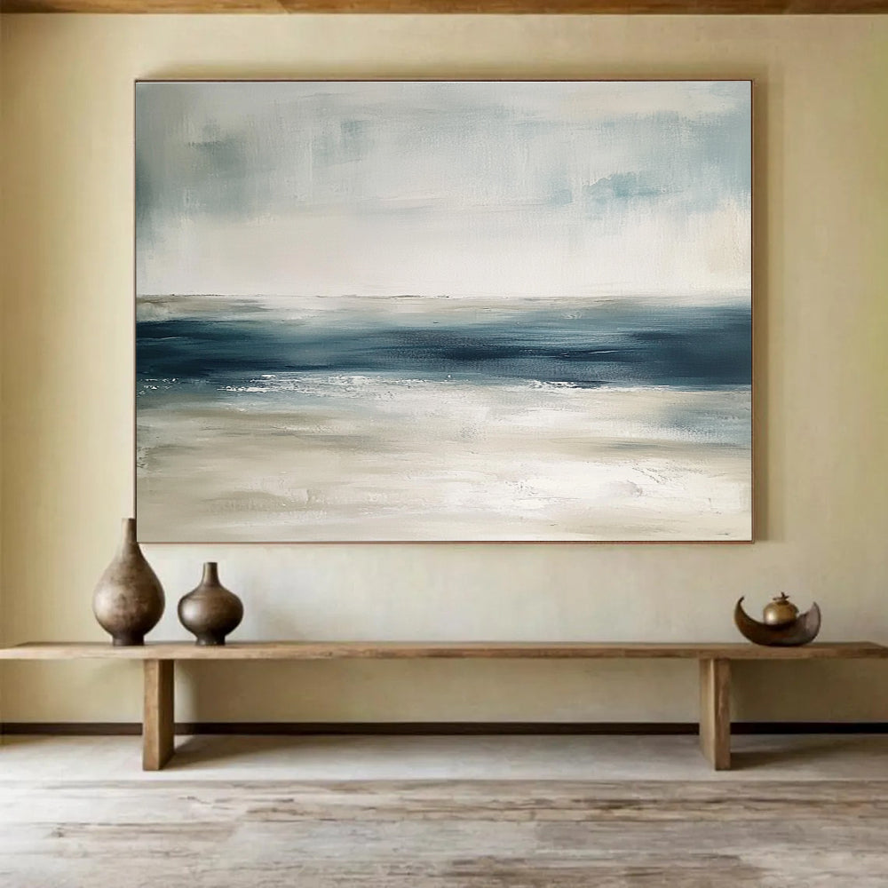 Large abstract painting featuring tranquil blue and gray tones with sandy beige hints soft brushstrokes evoke a serene ocean landscape.SC277