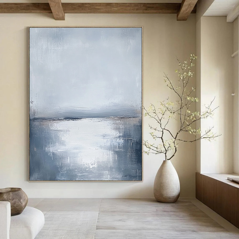 Large abstract painting featuring muted grays and soft blues capturing the serene connection between sunlit water and a cloudy sky.STSC464