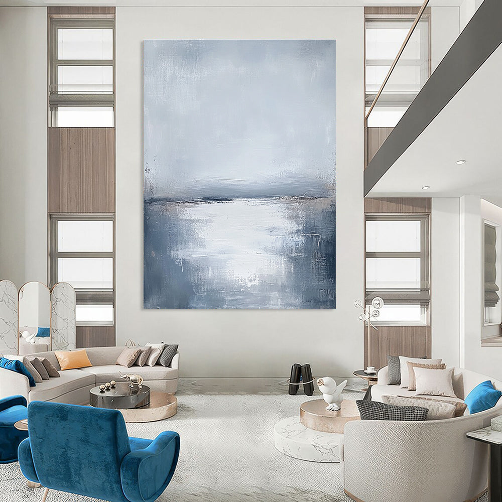 Large abstract painting featuring muted grays and soft blues capturing the serene connection between sunlit water and a cloudy sky.STSC464