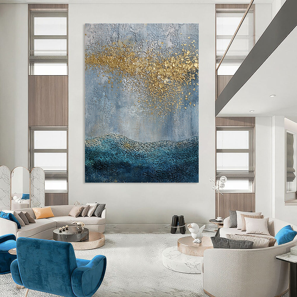 Large abstract painting with a textured sky-blue gray background and golden highlights featuring a textured sea with gentle waves in the foreground.STSC835