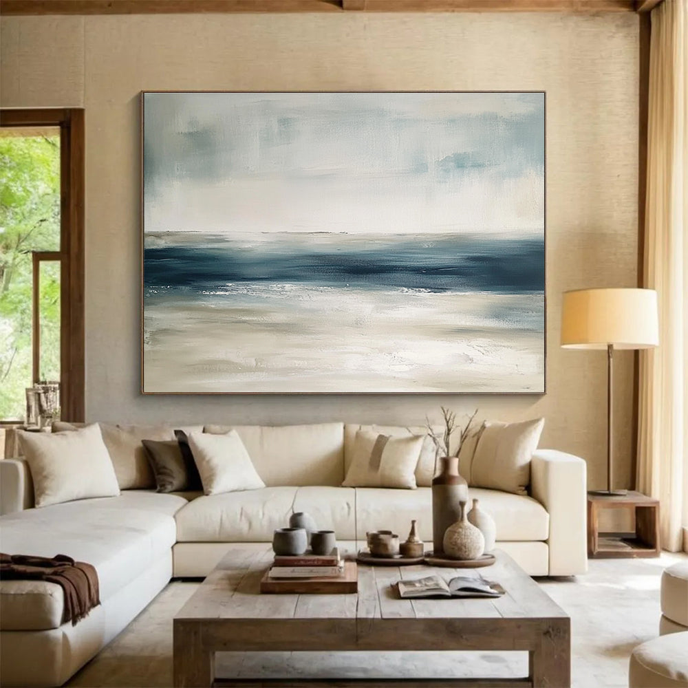 Large abstract painting featuring tranquil blue and gray tones with sandy beige hints soft brushstrokes evoke a serene ocean landscape.SC277