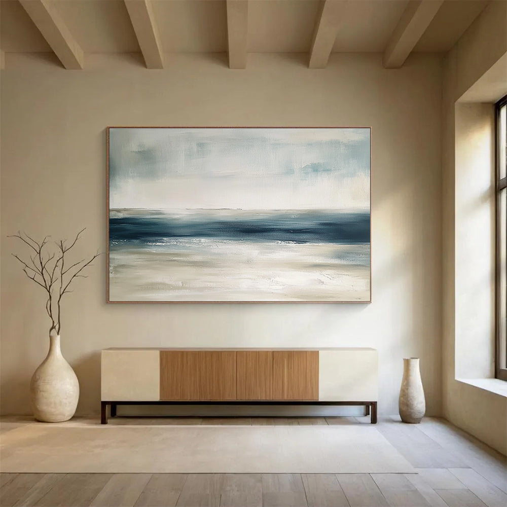 Large abstract painting featuring tranquil blue and gray tones with sandy beige hints soft brushstrokes evoke a serene ocean landscape.SC277