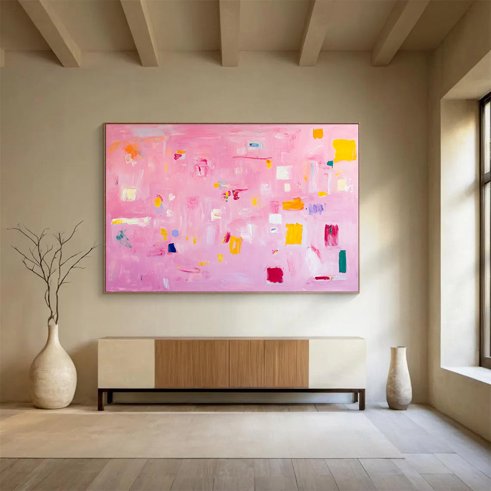 A large abstract painting featuring soft pink hues bright yellow blocks red lines and white squares creates a joyful warm atmosphere perfect for celebration.SC536