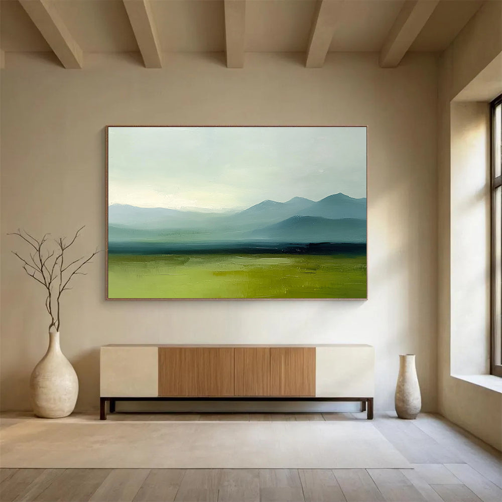 A large abstract oil painting depicting grassy plains and distant mountains in a minimalist style with a green and blue palette under a grey sky.SC409