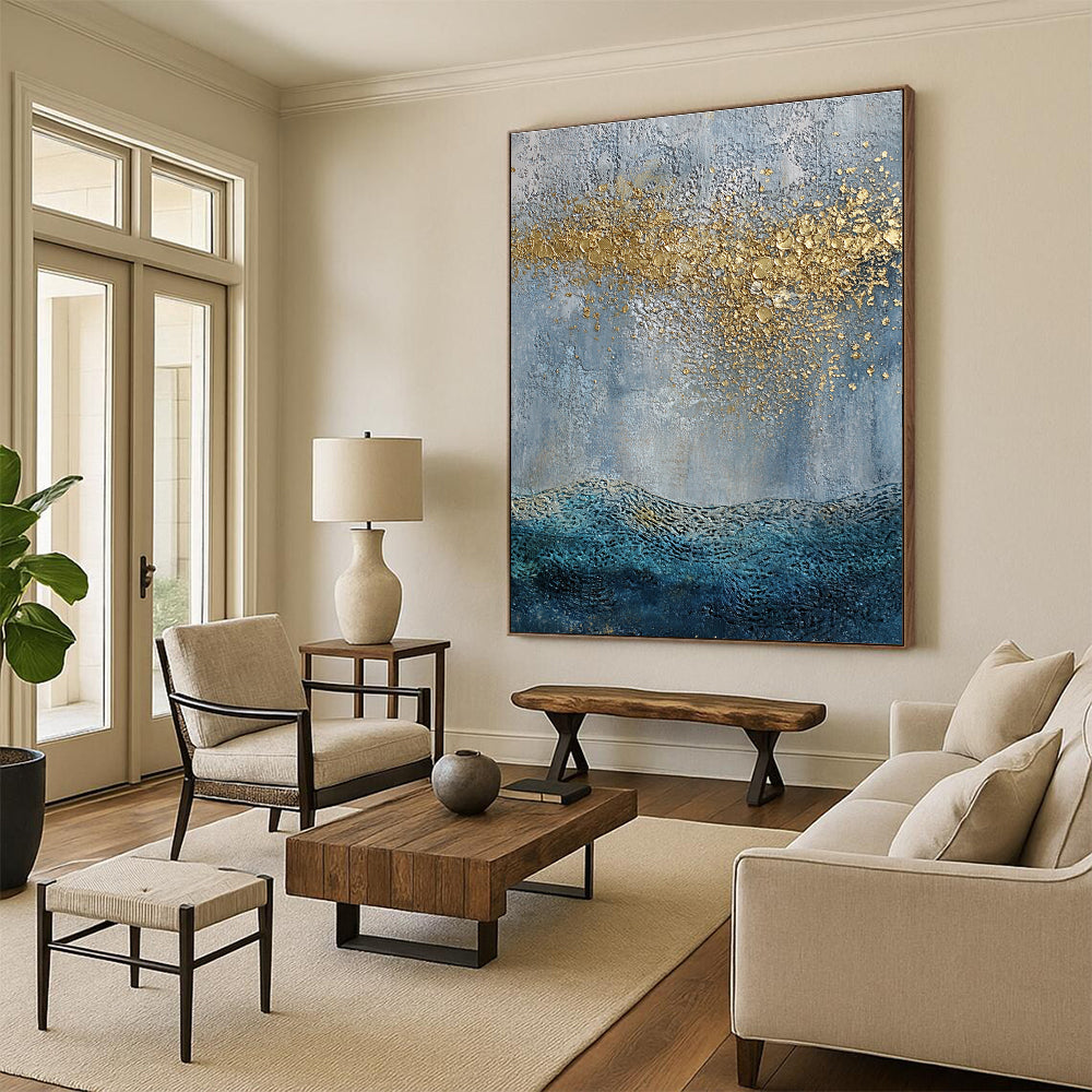 Large abstract painting with a textured sky-blue gray background and golden highlights featuring a textured sea with gentle waves in the foreground.STSC835