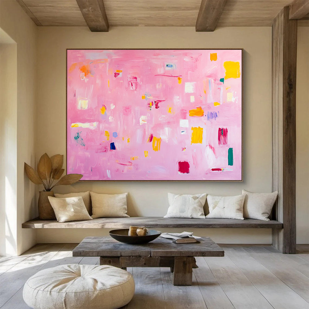 A large abstract painting featuring soft pink hues bright yellow blocks red lines and white squares creates a joyful warm atmosphere perfect for celebration.SC536