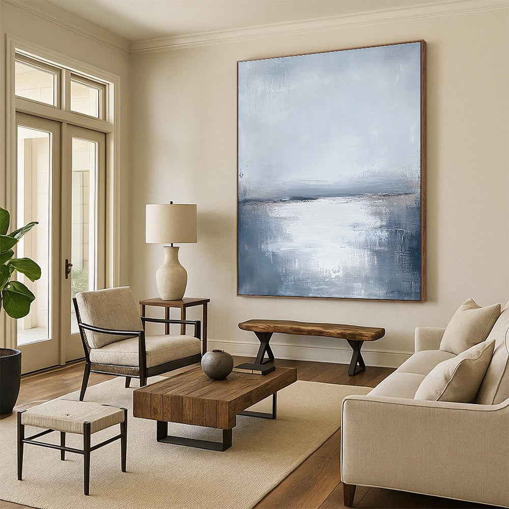 Large abstract painting featuring muted grays and soft blues capturing the serene connection between sunlit water and a cloudy sky.STSC464